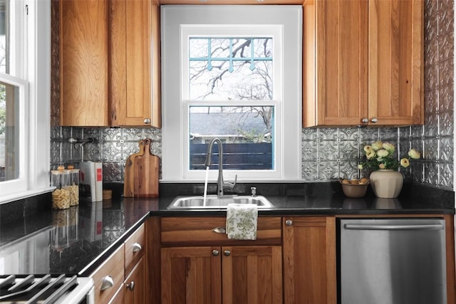 kitchen with stainless steel dishwasher, brown cabinetry, dark countertops, and a sink