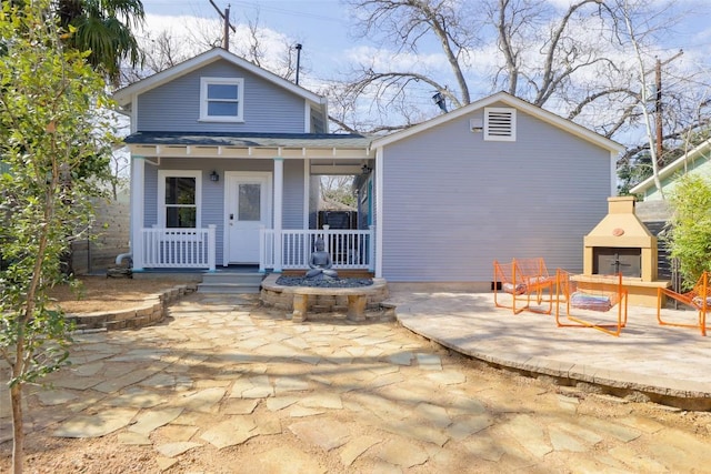 rear view of house with an outdoor fireplace, a porch, and a patio