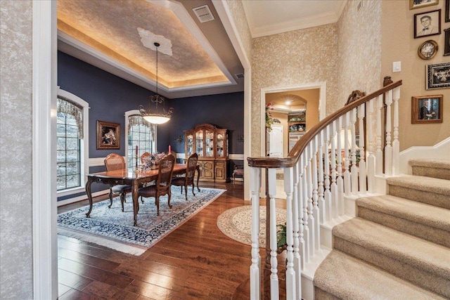 dining room featuring dark wood-type flooring, a raised ceiling, visible vents, and crown molding