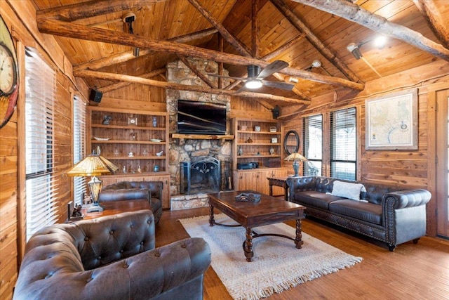 living room featuring a stone fireplace, wood finished floors, wood ceiling, and wooden walls