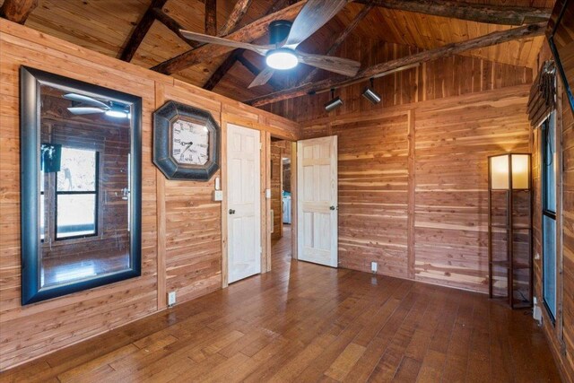 empty room with vaulted ceiling with beams, wooden ceiling, hardwood / wood-style flooring, and wooden walls