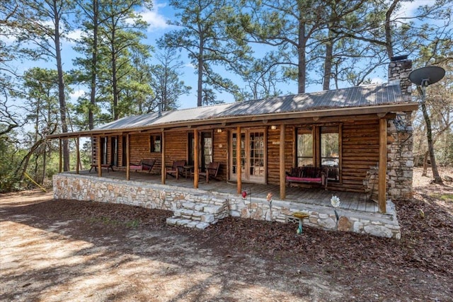 rear view of property with metal roof, a chimney, and a porch