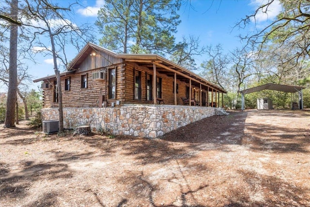 view of property exterior featuring central AC unit, covered porch, driveway, a detached carport, and log exterior