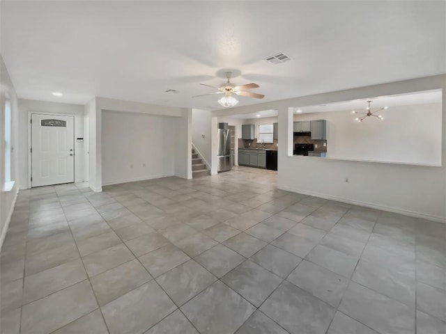 unfurnished living room featuring visible vents, stairway, baseboards, and ceiling fan with notable chandelier