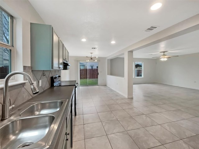 kitchen with visible vents, decorative backsplash, a sink, stainless steel electric range, and ceiling fan with notable chandelier