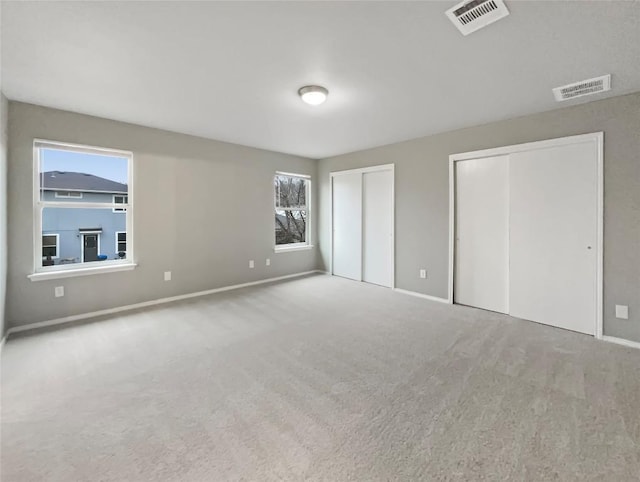 unfurnished bedroom featuring carpet, visible vents, and multiple closets