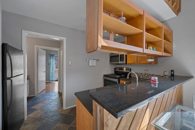 kitchen featuring a peninsula, a sink, baseboards, appliances with stainless steel finishes, and stone tile flooring