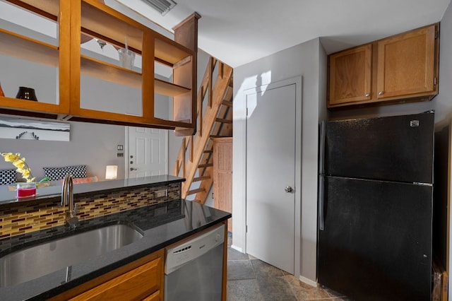 kitchen featuring dishwasher, brown cabinets, dark stone countertops, freestanding refrigerator, and a sink