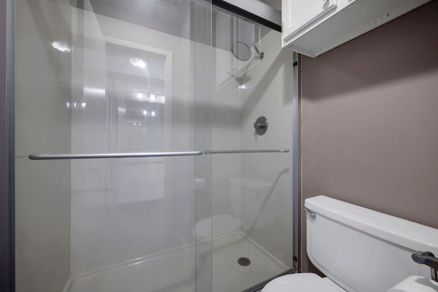 full bath with a textured wall, a shower stall, and toilet