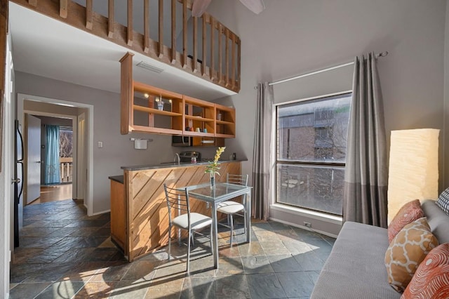 kitchen with a towering ceiling, a healthy amount of sunlight, visible vents, and stone tile flooring