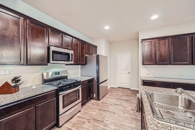 112 Quarton Dr, Hutto, TX 78634 - kitchen featuring appliances with stainless steel finishes, a sink, light wood finished floors, dark brown cabinetry, and tasteful backsplash