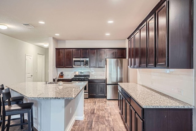112 Quarton Dr, Hutto, TX 78634 - kitchen with appliances with stainless steel finishes, a sink, light wood-style floors, tasteful backsplash, and dark brown cabinets