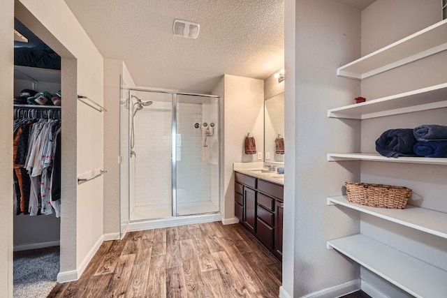 112 Quarton Dr, Hutto, TX 78634 - bathroom featuring a shower stall, a walk in closet, vanity, wood finished floors, and a textured ceiling