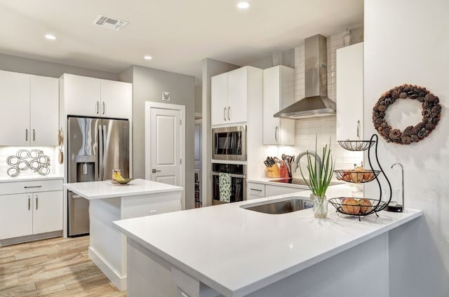 kitchen featuring stainless steel appliances, a peninsula, visible vents, wall chimney range hood, and tasteful backsplash