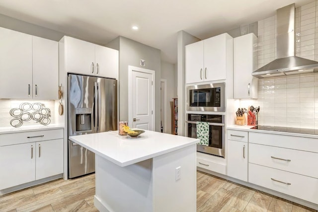 kitchen with light wood-type flooring, wall chimney range hood, tasteful backsplash, and appliances with stainless steel finishes