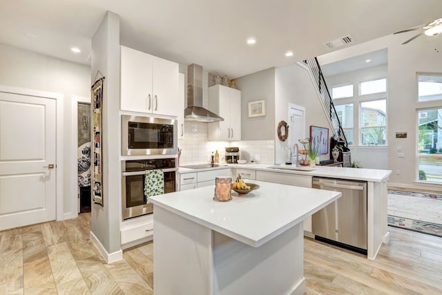 kitchen featuring a peninsula, a sink, visible vents, appliances with stainless steel finishes, and wall chimney exhaust hood