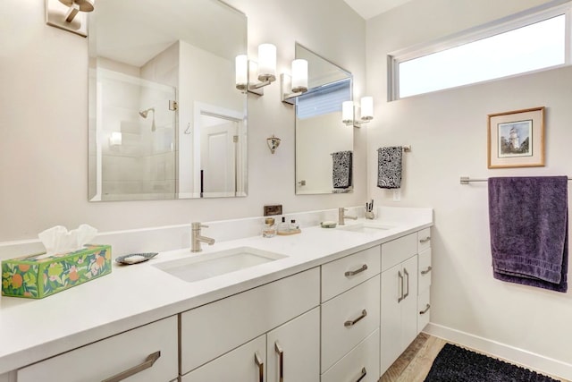 bathroom with double vanity, a stall shower, baseboards, and a sink