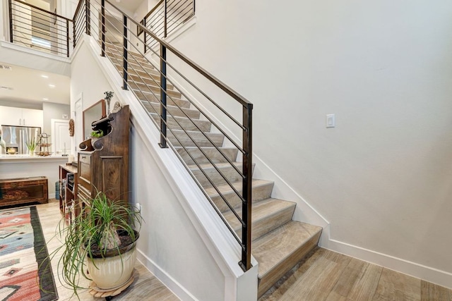 stairs with recessed lighting, baseboards, a high ceiling, and wood finished floors