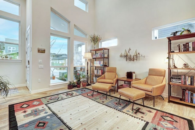 sitting room with wood finished floors, a towering ceiling, and baseboards