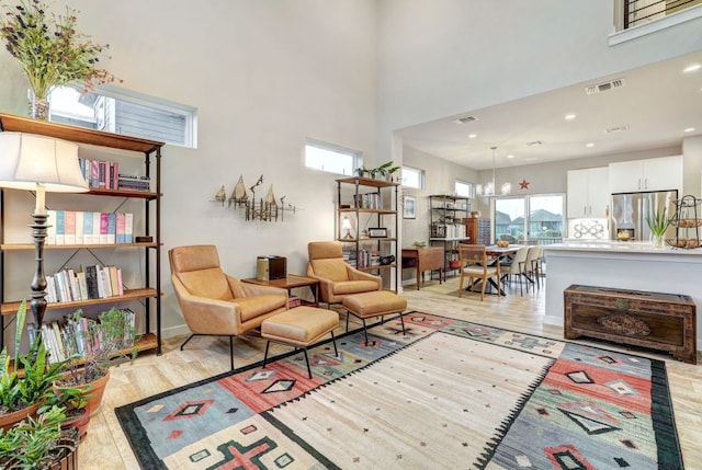 living area featuring visible vents, a towering ceiling, and light wood-style flooring