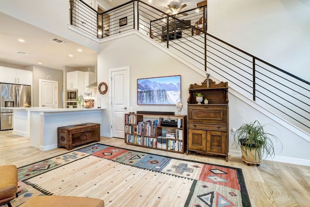 living room with light wood finished floors, visible vents, a towering ceiling, stairs, and recessed lighting