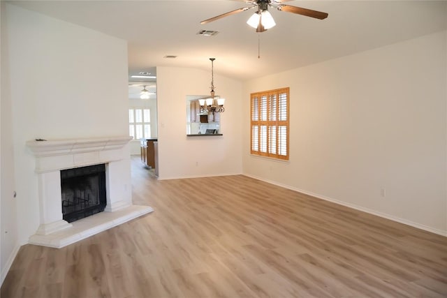 unfurnished living room featuring lofted ceiling, ceiling fan with notable chandelier, visible vents, a high end fireplace, and light wood finished floors