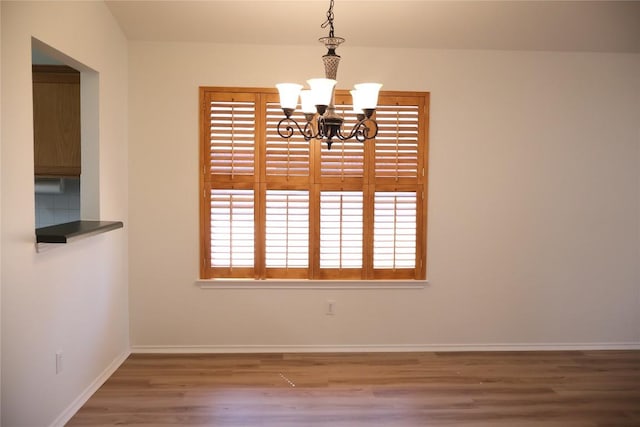 unfurnished dining area featuring a notable chandelier, baseboards, and wood finished floors