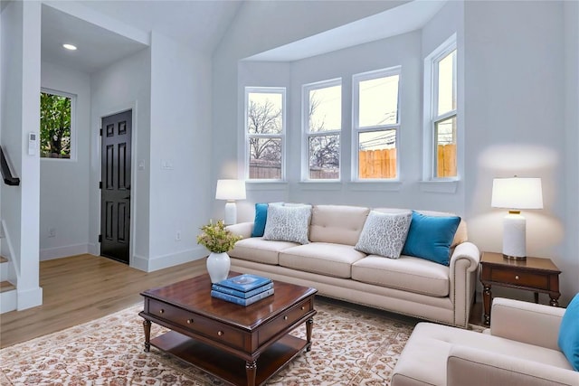 living room with stairs, light wood-type flooring, a wealth of natural light, and baseboards