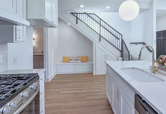 kitchen with light wood finished floors, dishwasher, under cabinet range hood, white cabinetry, and a sink