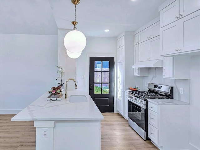 kitchen with stainless steel gas stove, light wood finished floors, under cabinet range hood, white cabinetry, and a sink