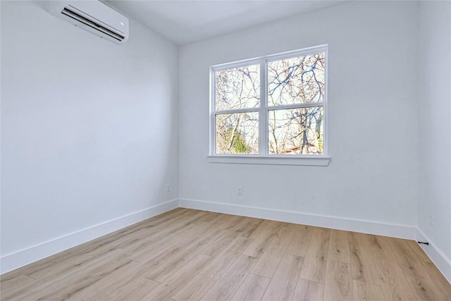 spare room featuring light wood finished floors, baseboards, and a wall mounted AC