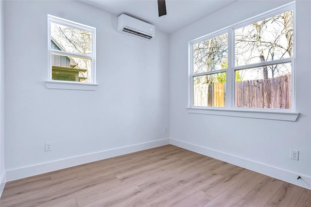 empty room with a ceiling fan, an AC wall unit, light wood-style flooring, and baseboards