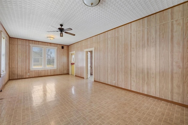 spare room with brick patterned floor, wood walls, a ceiling fan, and baseboards