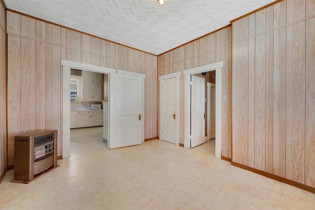 spare room with wood walls, baseboards, ornamental molding, heating unit, and light floors