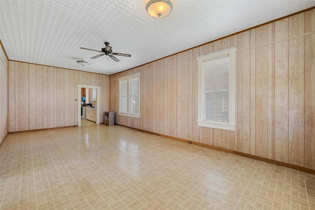 spare room with brick patterned floor, wood walls, a ceiling fan, and baseboards
