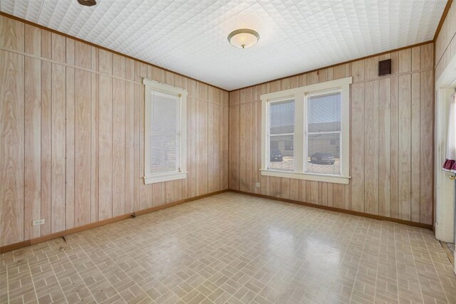 spare room with brick patterned floor, wood walls, and baseboards