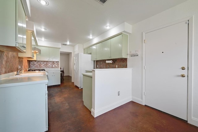 kitchen with tasteful backsplash, freestanding refrigerator, a peninsula, concrete flooring, and a sink