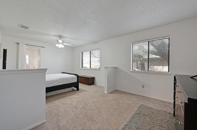 carpeted bedroom with a textured ceiling, baseboards, a ceiling fan, and visible vents