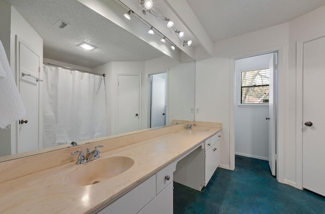 bathroom featuring a textured ceiling, double vanity, a sink, and visible vents