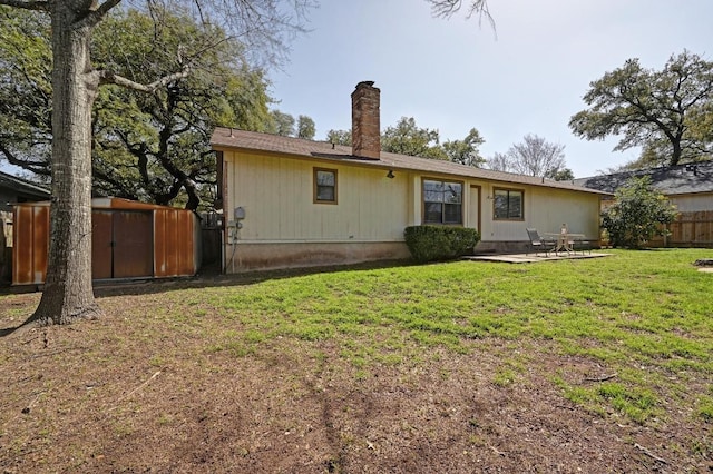 back of house with a lawn, a chimney, fence, a patio, and an outbuilding