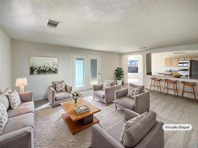 living area with light carpet, visible vents, arched walkways, baseboards, and a textured ceiling