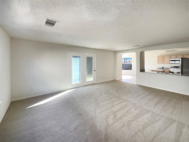 unfurnished living room with arched walkways, visible vents, carpet flooring, a sink, and a textured ceiling