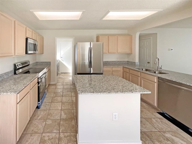 kitchen with a center island, light tile patterned floors, stainless steel appliances, light brown cabinets, and a sink