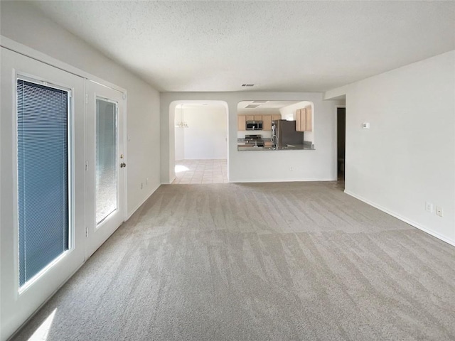 unfurnished living room featuring arched walkways, a textured ceiling, baseboards, and light colored carpet