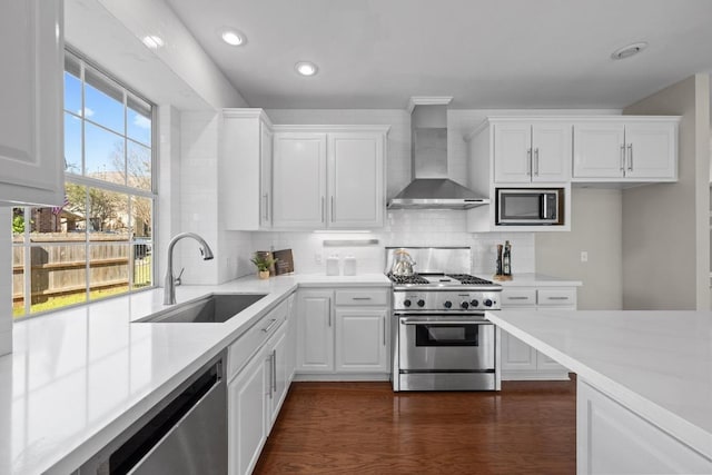 kitchen with stainless steel appliances, light countertops, backsplash, a sink, and wall chimney exhaust hood