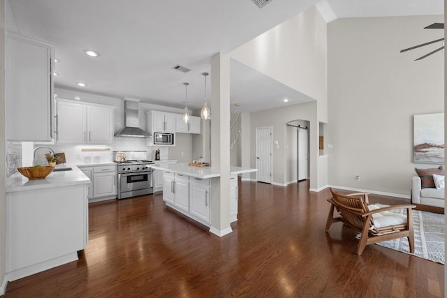 kitchen featuring visible vents, appliances with stainless steel finishes, light countertops, wall chimney range hood, and a sink