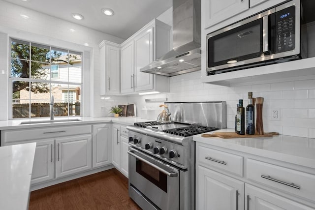 kitchen with stainless steel appliances, white cabinetry, light countertops, wall chimney range hood, and dark wood finished floors