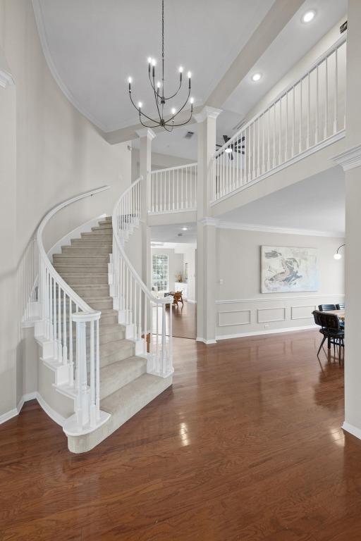 entrance foyer featuring a notable chandelier, a high ceiling, ornamental molding, wood finished floors, and stairs