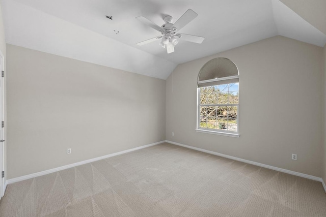 spare room featuring light carpet, vaulted ceiling, a ceiling fan, and baseboards