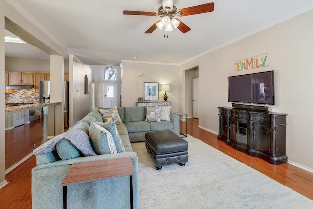 living area featuring baseboards, ornamental molding, ceiling fan, and wood finished floors